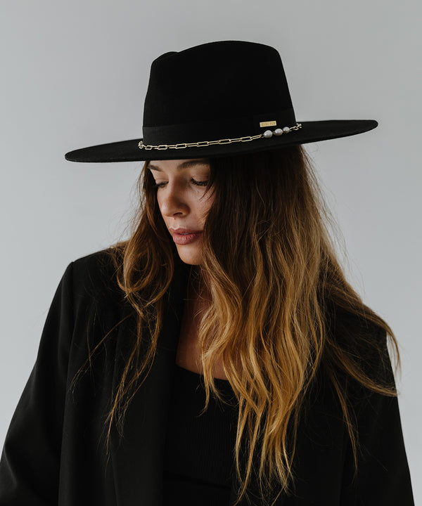 Gigi Pip felt hats for women - Raine Wide Brim Fedora - wide flat brim with a fedora crown, featuring a gold-plated removable paperclip brass chain with three faux pearls and a hand-sewn grosgrain band with the gold Gigi Pip bar around the crown, as well as a removable golden chain chinstrap [black]